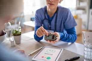 看護師、介護者、または医療従事者と高齢の女性患者が、屋内で血糖値を測定します。