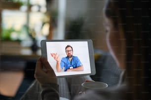 Jeune femme malade ayant un appel vidéo avec un médecin sur tablette à domicile, concept de consultation en ligne.