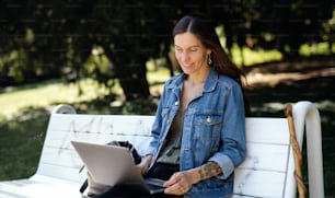 Femme mûre avec un ordinateur portable assise sur un banc à l’extérieur dans un parc de la ville ou de la ville, travaillant.