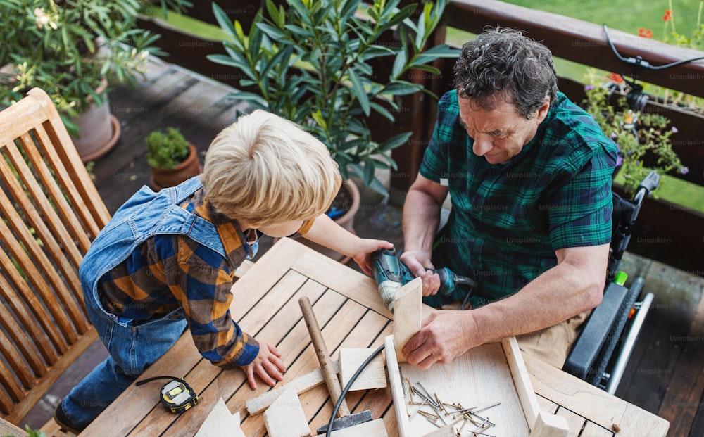 Vue de dessus d’un petit garçon heureux avec un grand-père aîné en fauteuil roulant construisant un nichoir, projet de bricolage.