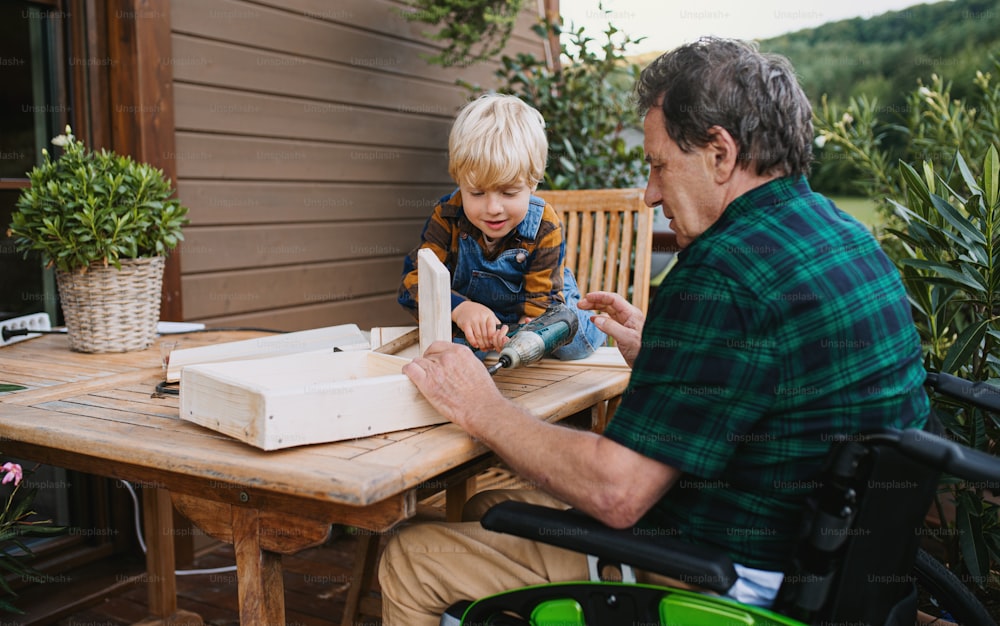 Petit garçon heureux avec grand-père aîné en fauteuil roulant construisant un nichoir, projet de bricolage.