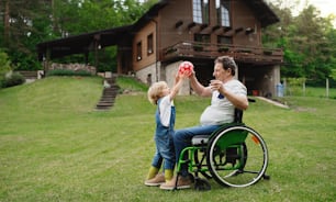 Petit garçon heureux avec grand-père aîné en fauteuil roulant dans le jardin, jouant avec un ballon.