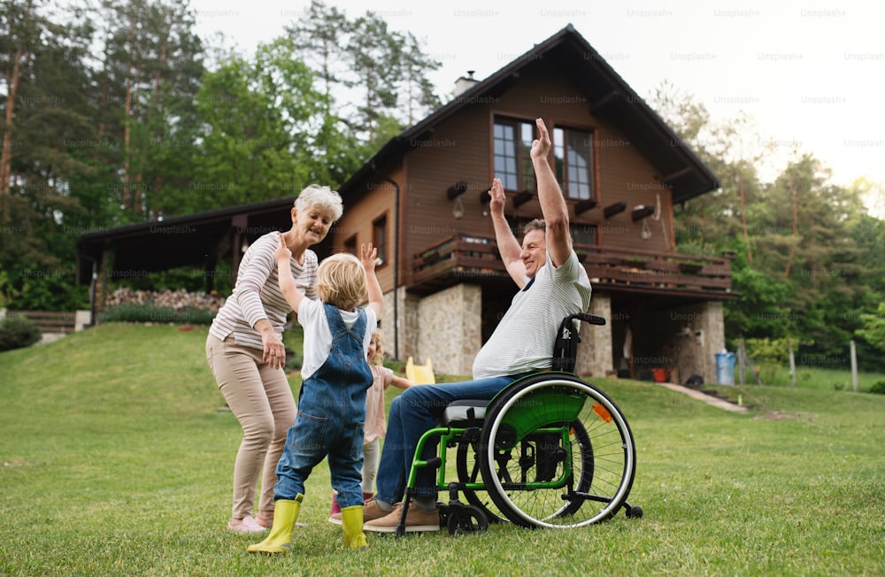 Niños pequeños felices con abuelos mayores en silla de ruedas jugando.