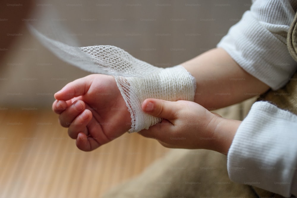 Hände von unkenntlich verletzt kleines Kleinkind mit Verband drinnen zu Hause.