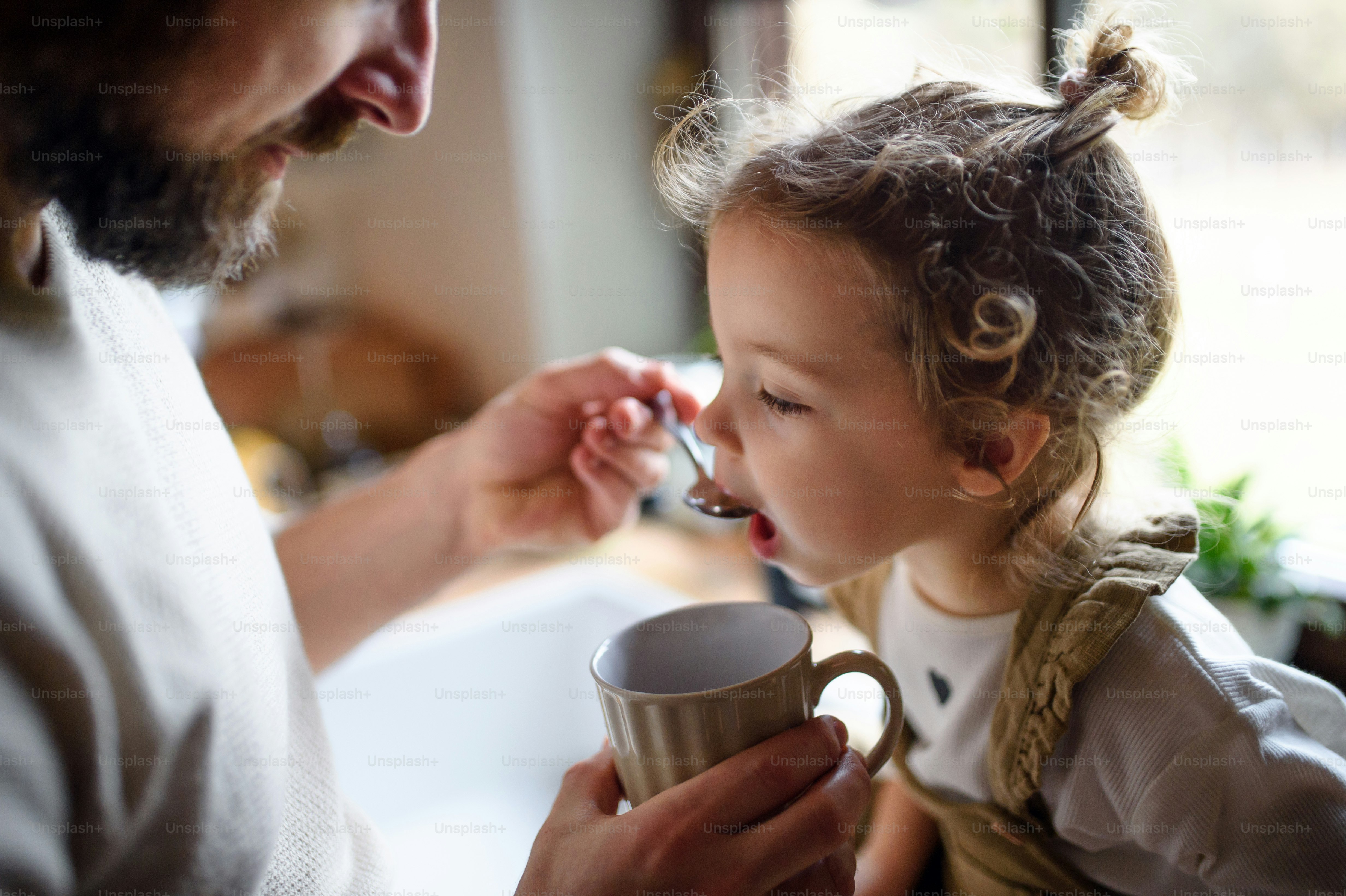 Nicht wiederzuerkennender reifer Vater, der einer kleinen kranken Tochter zu Hause Sirup gibt.