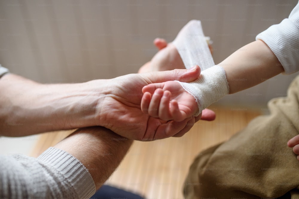 認識できない父親が、自宅の屋内で小さな傷ついた幼児の子供に包帯を巻く。