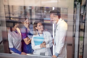 Group of doctors in elevator on medical conference, talking. Shot through glass.