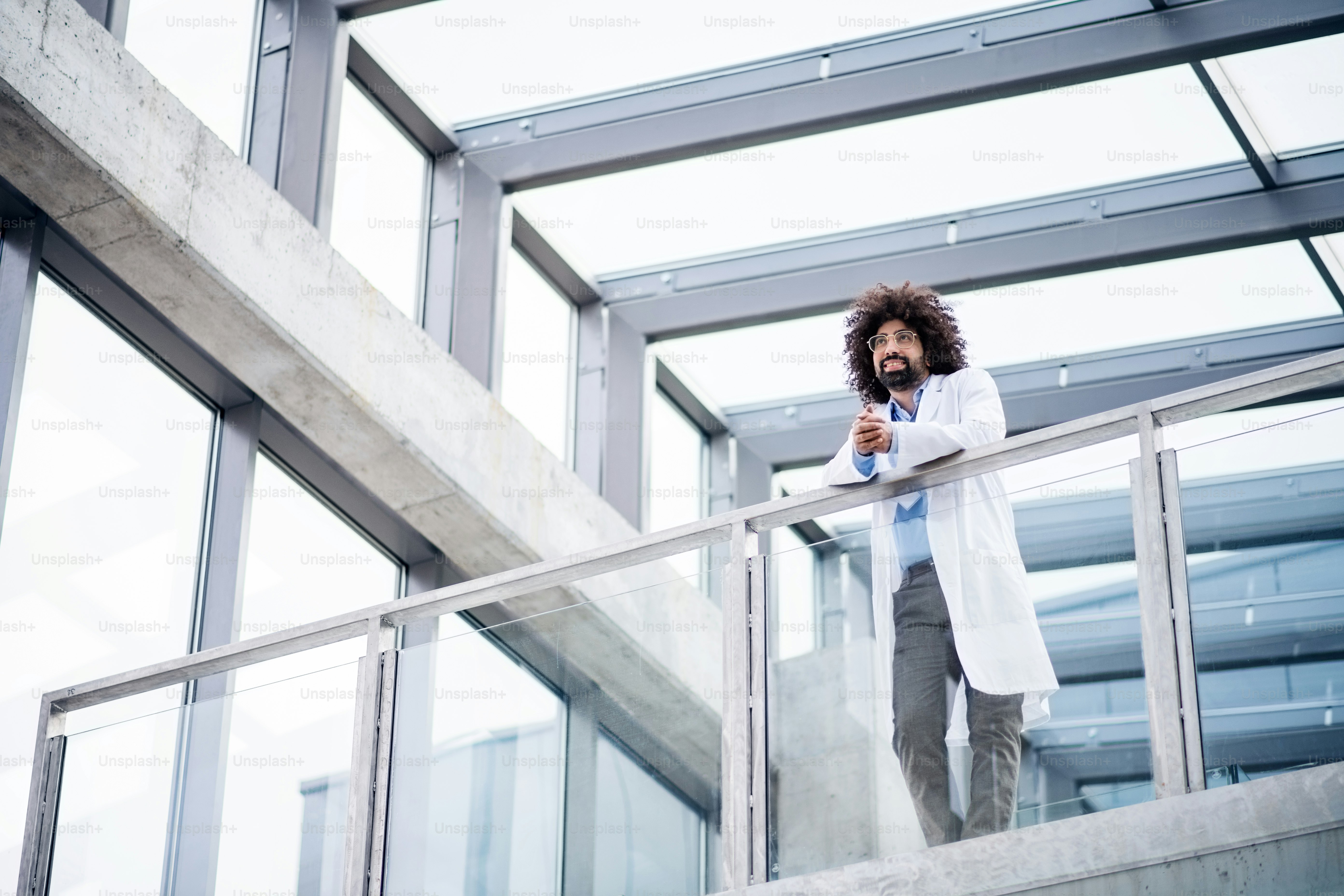 Ritratto di medico maschio in piedi sul corridoio, appoggiato alla ringhiera. Copia spazio.