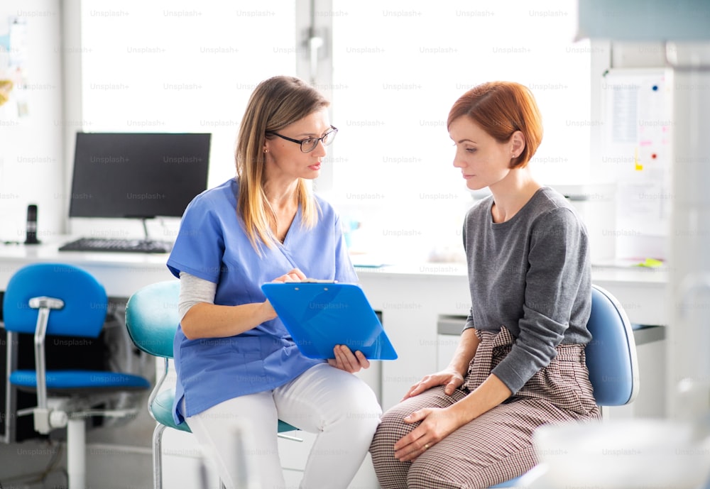 Um dentista com prancheta conversando com mulher em cirurgia de dentista, um check-up odontológico.