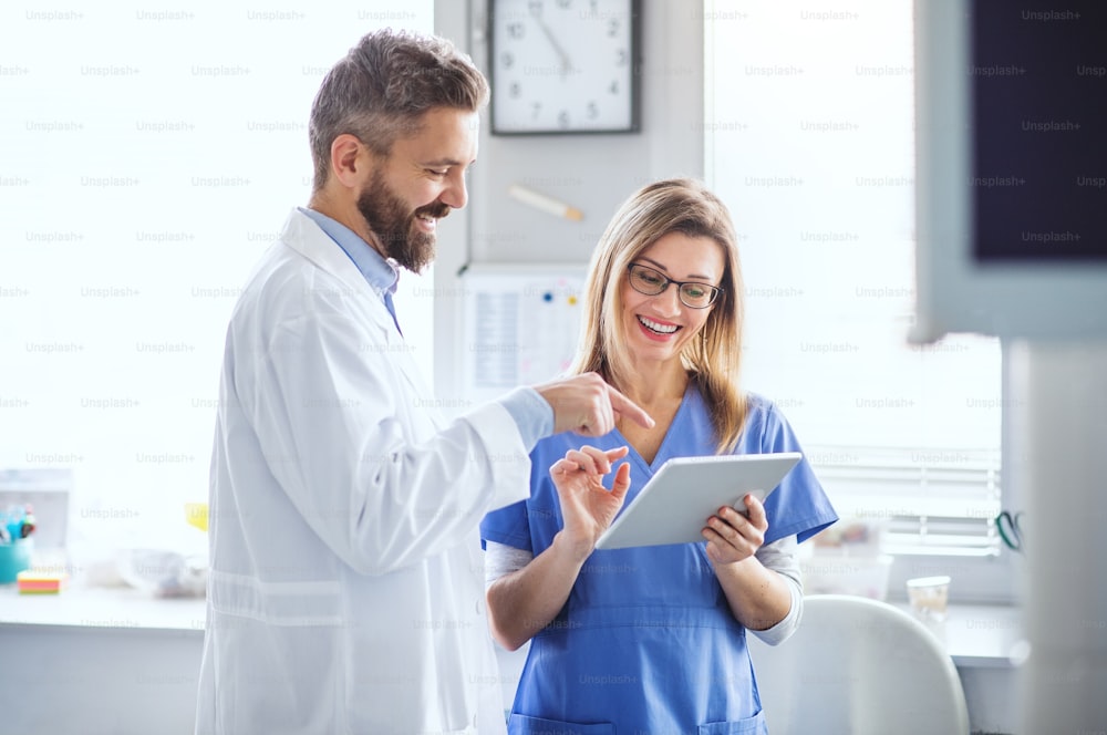 A front view portrait of dental assistant and dentist in modern dental surgery, using tablet.