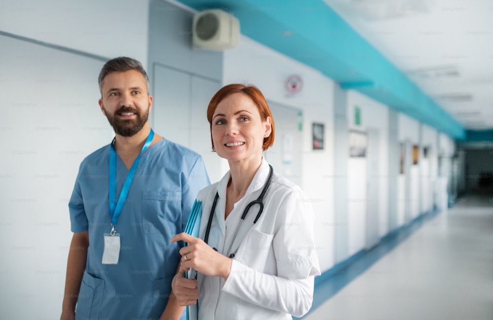 Portrait of man and woman doctor walking in hospital, looking at camera. Copy space.