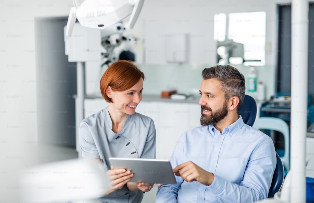 Front view of man and dentist with tablet in dental surgery, annual check-up.