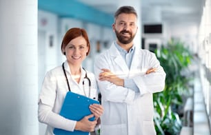 Un retrato de un médico y una doctora de pie en el hospital, mirando a la cámara.