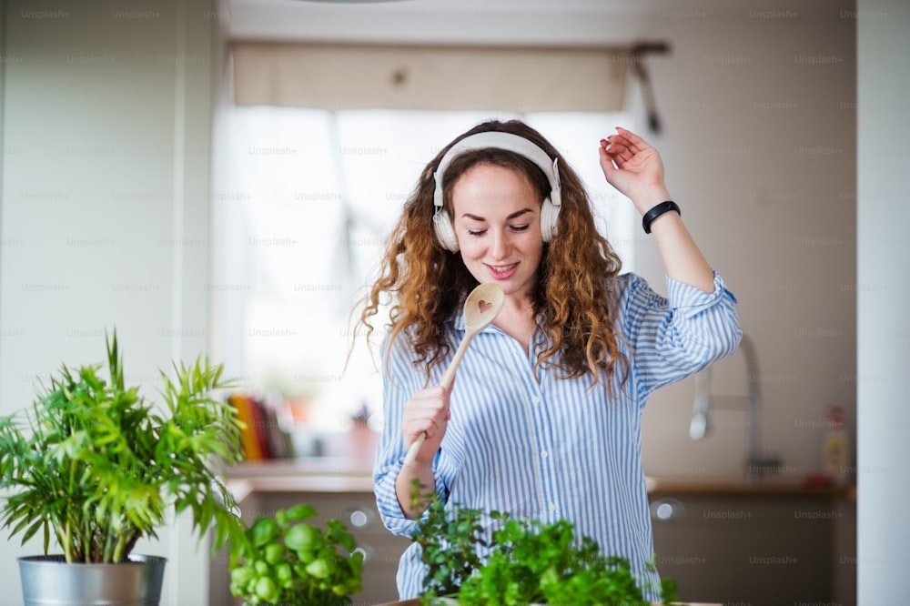 Mujer joven con auriculares relajándose en el interior de su casa, escuchando música y cantando.