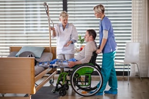 Mujeres trabajadoras de la salud y pacientes mayores en silla de ruedas en el hospital, hablando.