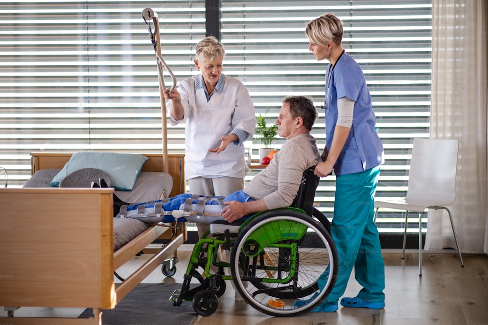 Women healthcare workers and senior patient in wheelchair in hospital, talking.