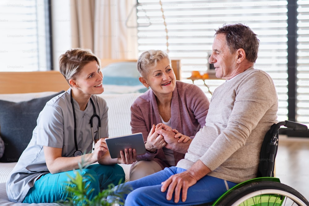 A healthcare worker with tablet visiting senior patient in wheelchair at home, talking.