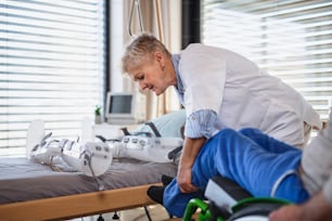 A healthcare worker and man paralysed senior patient in hospital, applying orthosis.