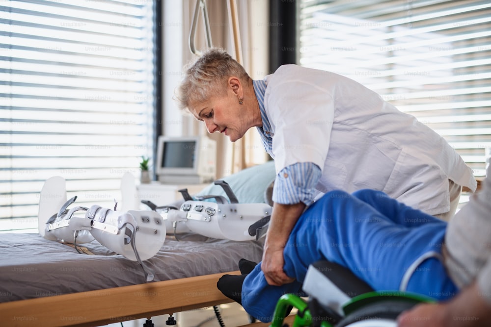 A healthcare worker and man paralysed senior patient in hospital, applying orthosis.
