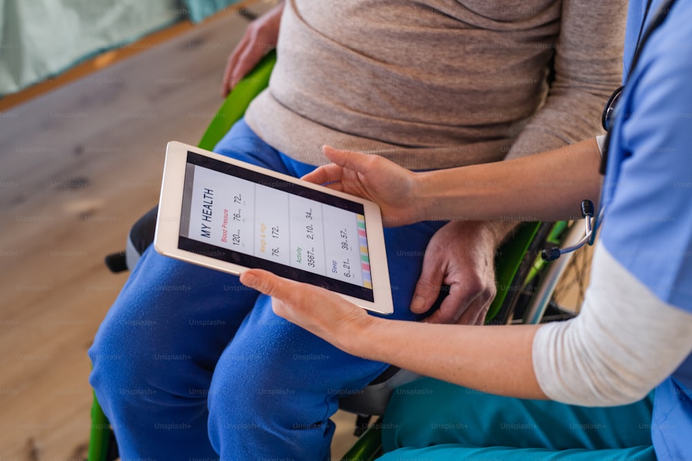 Una sección media de médico con tableta y paciente en silla de ruedas en el hospital, hablando.