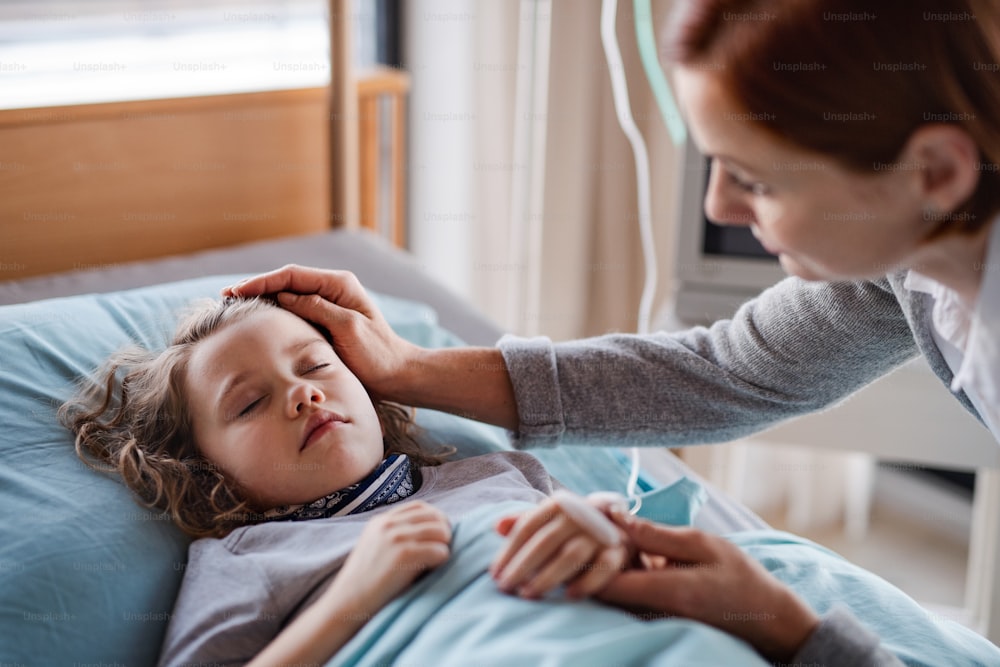 Caring mother visiting sleeping small girl daughter in bed in hospital.