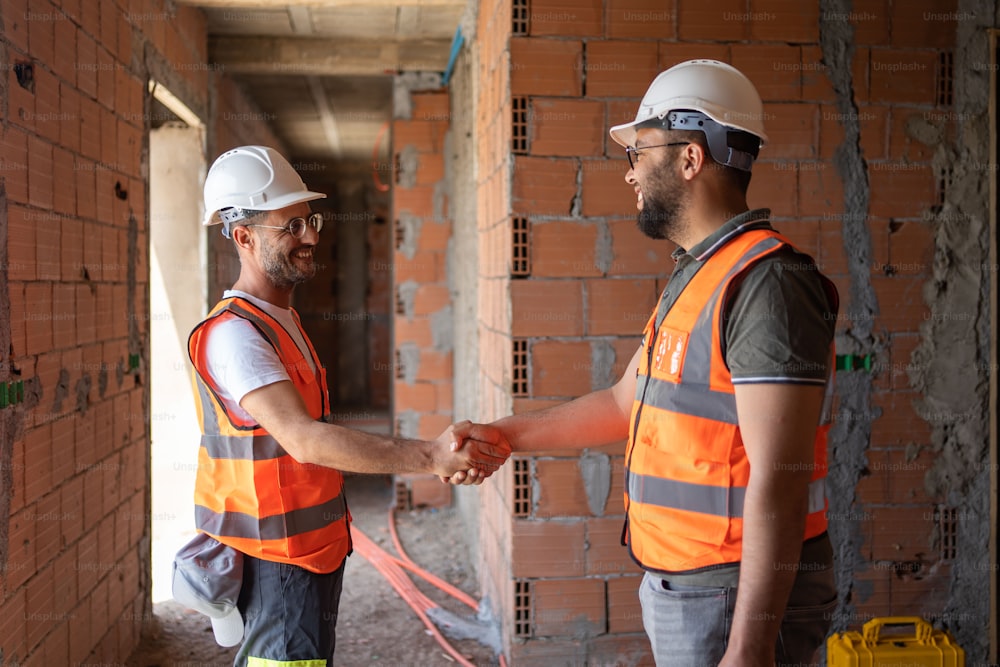 two construction workers shaking hands in front of a brick wall