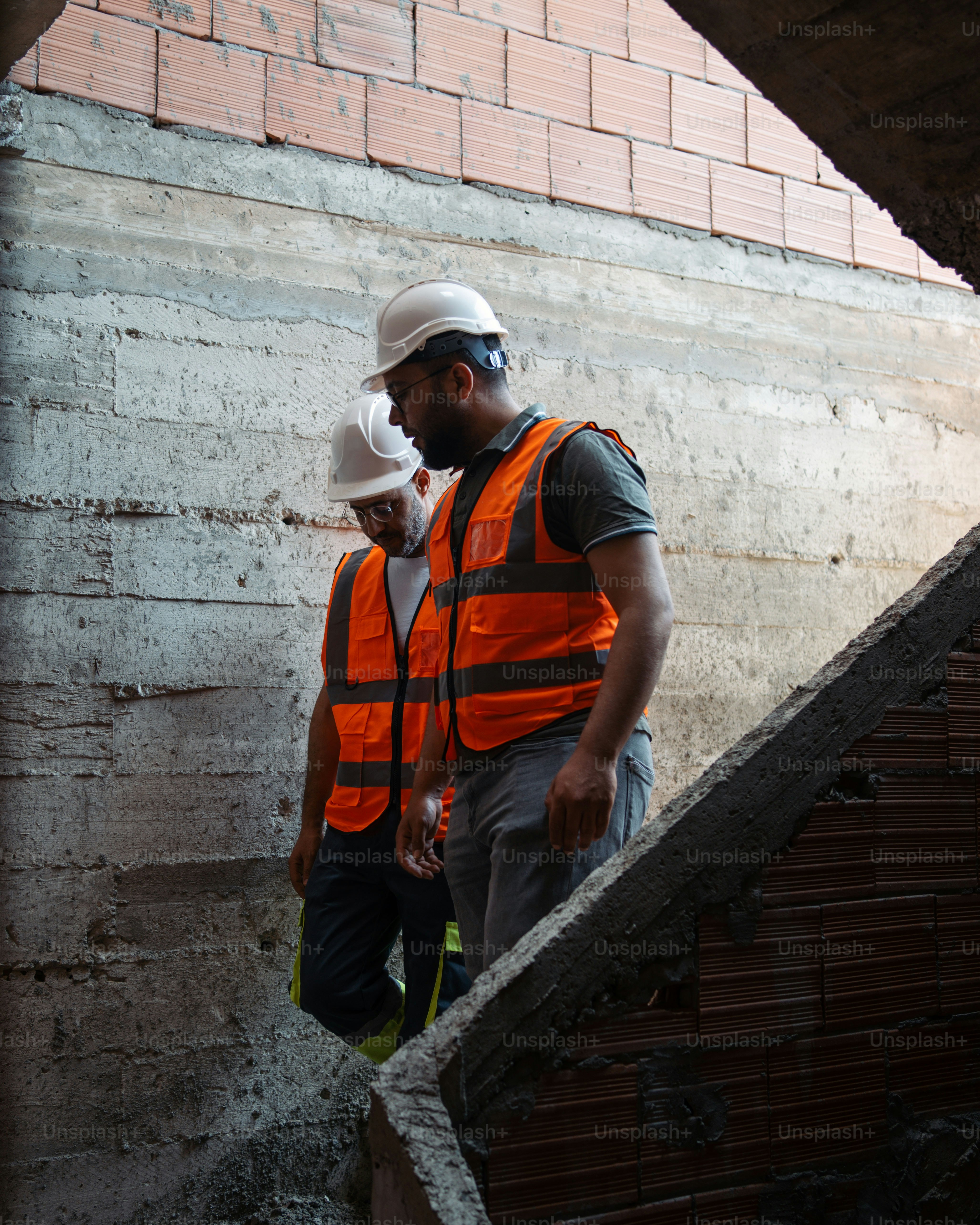 Ein Mann mit Schutzhelm und Weste, der neben einer Ziegelmauer steht