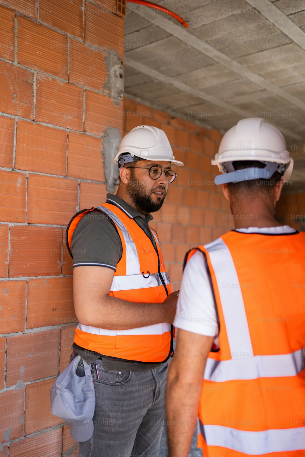 two construction workers standing next to a brick wall