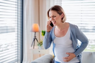 Un portrait d’une femme enceinte souffrant à l’intérieur à la maison, faisant un appel d’urgence.