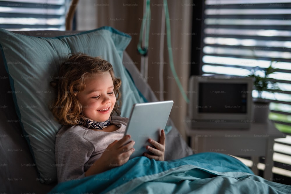 태블릿을 사용하여 병원에서 침대에 누워 있는 지루한 어린 소녀.