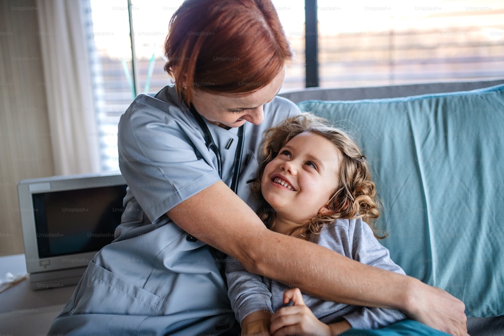 Medico femminile amichevole con stetoscopio che parla con la bambina nel letto in ospedale.