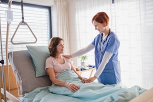 Friendly female doctor examining patient in bed in hospital.