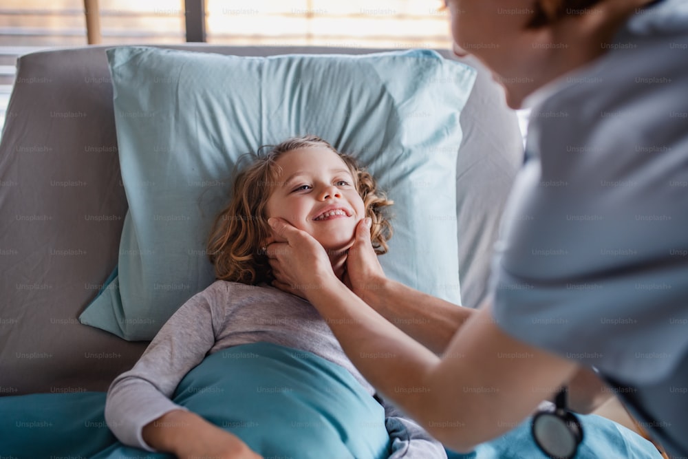 Friendly female doctor with stethoscope examining small girl in bed in hospital.