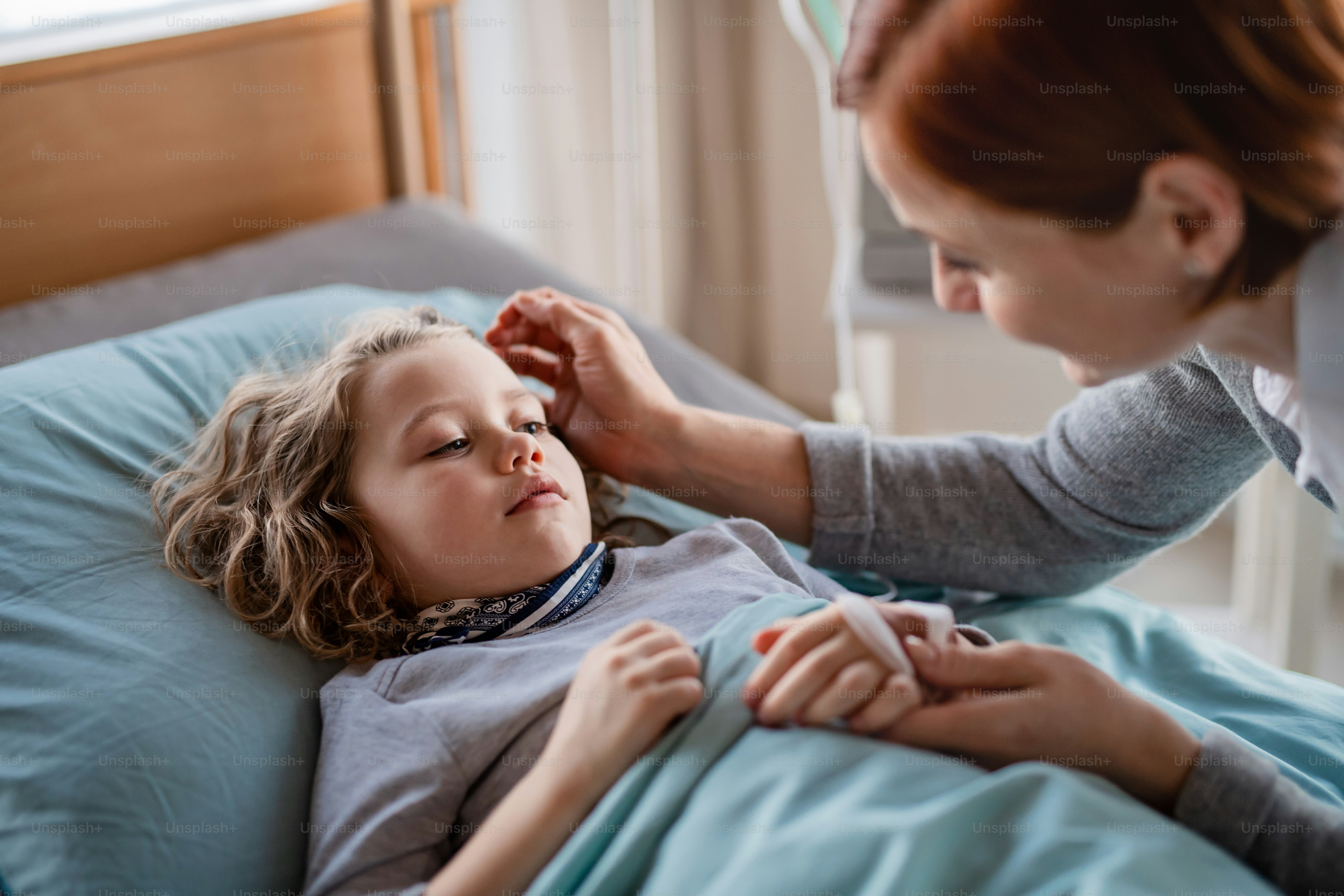 Eine fürsorgliche Mutter, die ihre kleine Tochter im Bett im Krankenhaus besucht.
