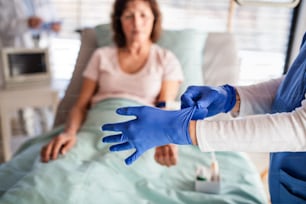 An unrecognizable doctor with patient in bed in hospital, putting on gloves.