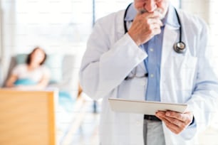 Un medico maschio anziano irriconoscibile in piedi nella stanza d'ospedale, usando un tablet.
