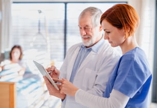 Portrait of senior male doctor standing in hospital room, talking to a female nurse.