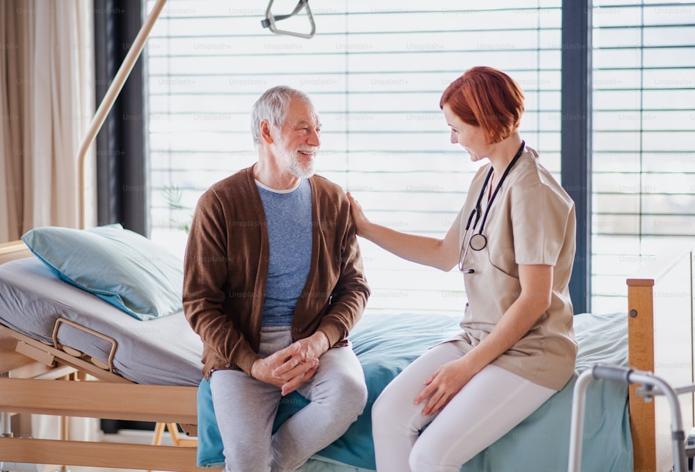 Una amable doctora hablando con un paciente mayor en la cama del hospital.