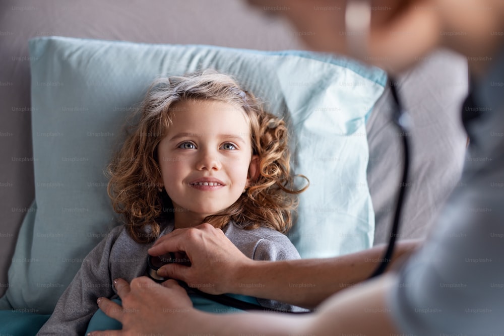 청진기를 가진 알아볼 수 없는 여성 의사가 병원 침대에서 어린 소녀를 검사하고 있다.