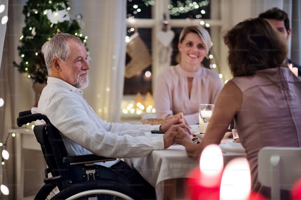 Homem idoso feliz em cadeira de rodas com a família dentro de casa celebrando o Natal juntos.
