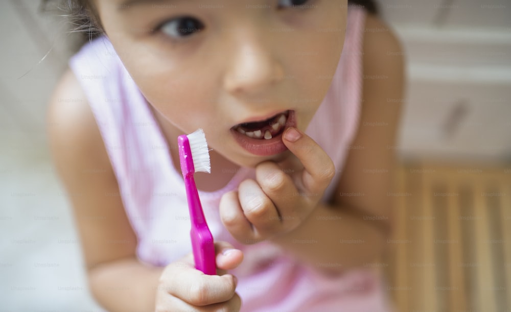 Draufsicht Porträt eines besorgten kleinen Mädchens mit Zahnbürste drinnen, das Milchzahn verliert.