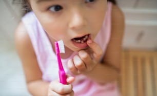 Retrato de vista superior de una niña pequeña preocupada con un cepillo de dientes en el interior, perdiendo un diente de leche.