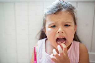 Retrato frontal de una niña pequeña preocupada con un cepillo de dientes en el interior, perdiendo un diente de leche.