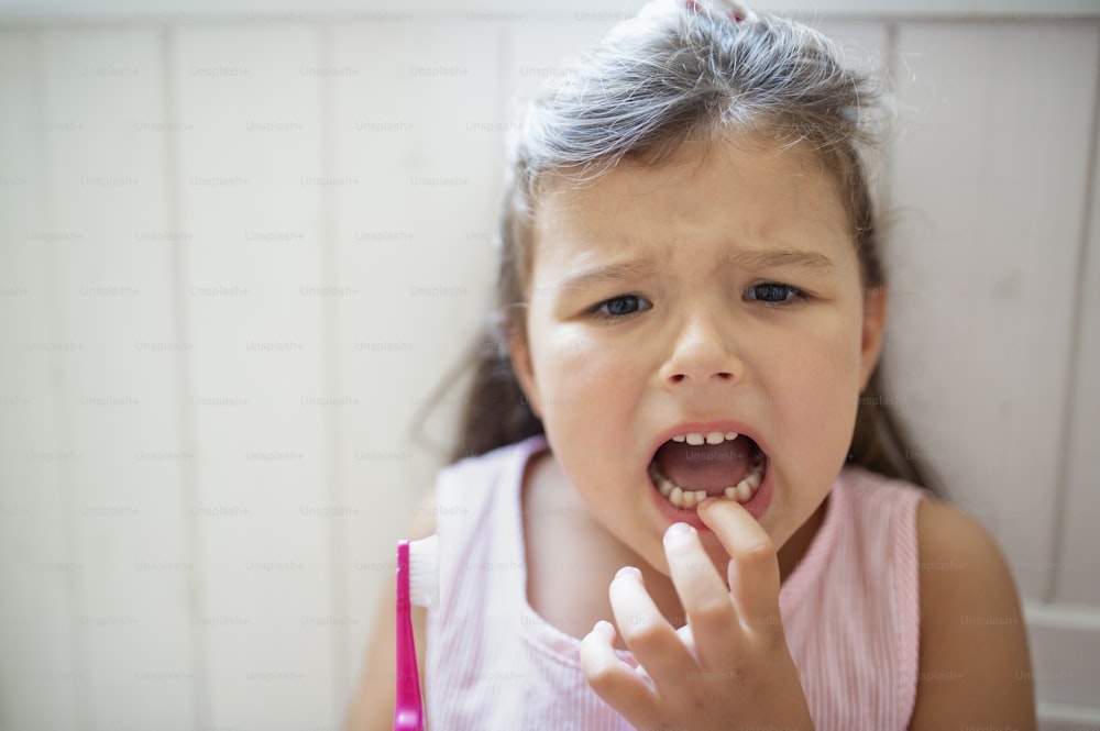 Vorderansicht Porträt eines besorgten kleinen Mädchens mit Zahnbürste in Innenräumen, das Milchzahn verliert.