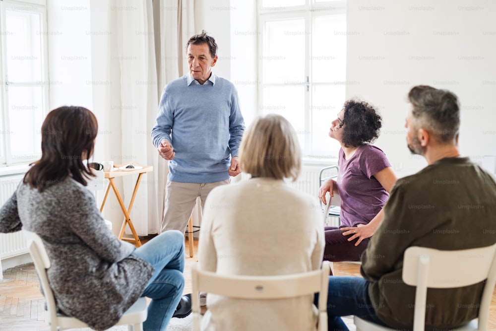 A mature man standing and talking to other people during group therapy.
