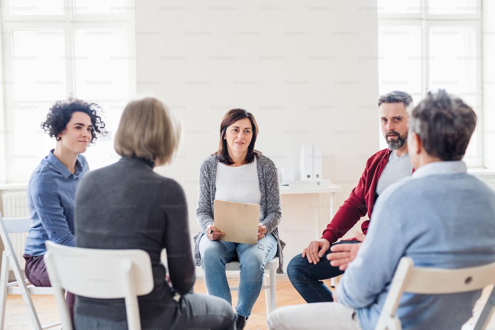 Serious men and women sitting in a circle during group therapy, talking.