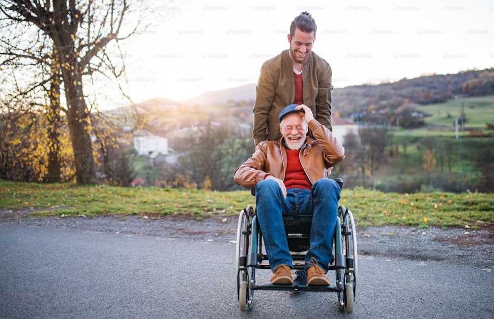 A young man and his senior father in wheelchair on a walk in town at sunset.