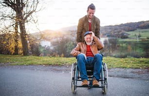 A young man and his senior father in wheelchair on a walk in town at sunset.