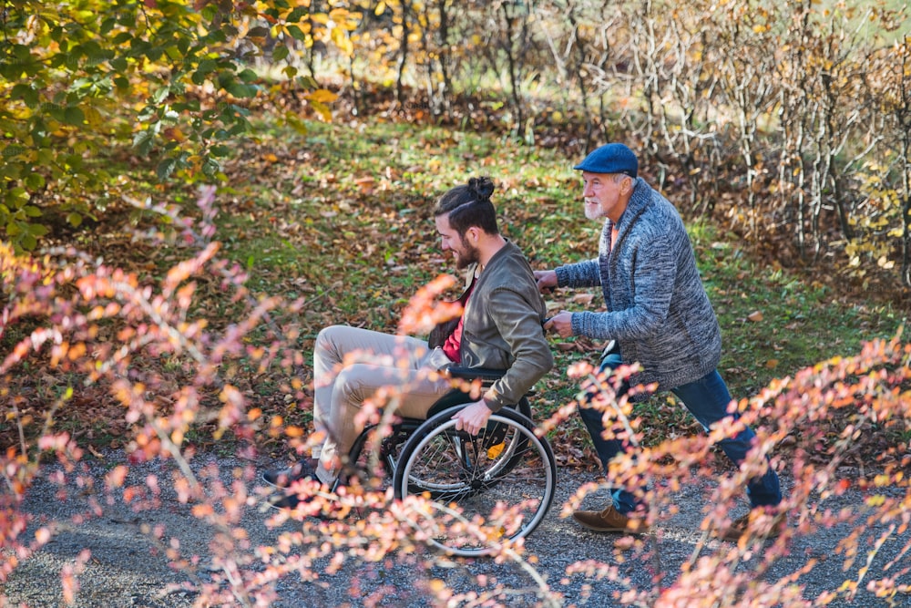 Un padre mayor y su hijo en silla de ruedas caminando por la naturaleza.
