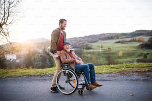 Un joven y su padre mayor en silla de ruedas en un paseo por la ciudad al atardecer.